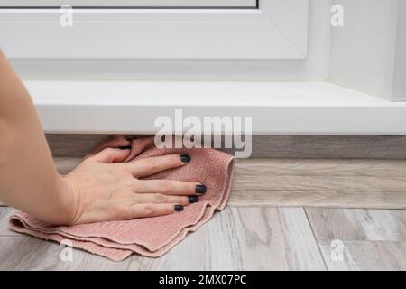 Eine Frau wäscht den Boden an einem schwer erreichbaren Ort. Wischen Sie die Fußleiste mit einem Lappen ab. Hausreinigung. Stockfoto