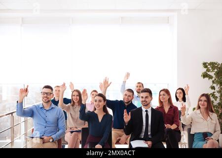 Menschen, die sich bei Geschäftsschulungen in geschlossenen Räumen die Hand heben, um Fragen zu stellen Stockfoto