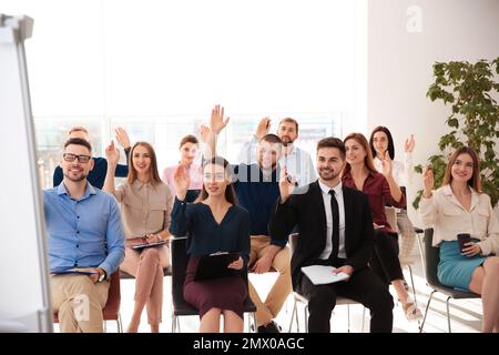 Menschen, die sich bei Geschäftsschulungen in geschlossenen Räumen die Hand heben, um Fragen zu stellen Stockfoto