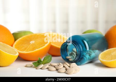 Flasche mit Vitaminpillen und Orange auf weißem Holztisch Stockfoto