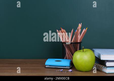 Komposition mit Schreibwaren und Apfel auf dem Tisch neben dem Schwarzen Brett, Platz für Text. Hausaufgaben machen Stockfoto