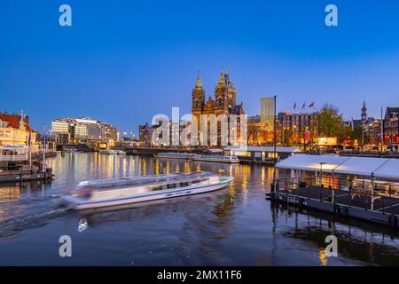 Blick über den Hafen von der Centraal Station IJzijde über den Hafen in Richtung St. Nicholas Kirche und Prins Hendrikkade Straße in der Abenddämmerung Stockfoto