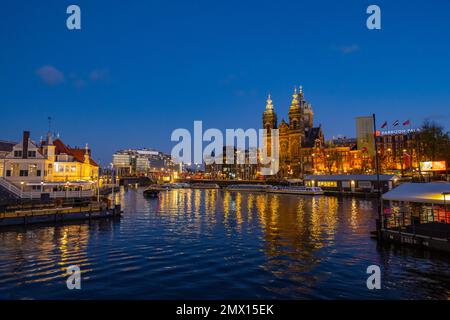 Blick über den Hafen von der Centraal Station IJzijde über den Hafen in Richtung St. Nicholas Kirche und Prins Hendrikkade Straße in der Abenddämmerung Stockfoto