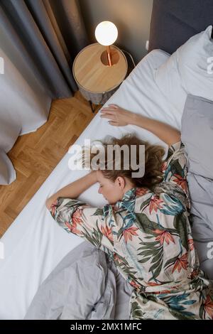 Junge Brünette zwischen zerknitterten Laken in einem Kingsize-Bett Stockfoto