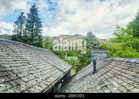 Elterwater, English Lake District, Cumbria, England, Großbritannien - mit Blick auf Schieferfliesen und Schornsteine von Ferienhüttendächern in Richtung der Hügel Stockfoto