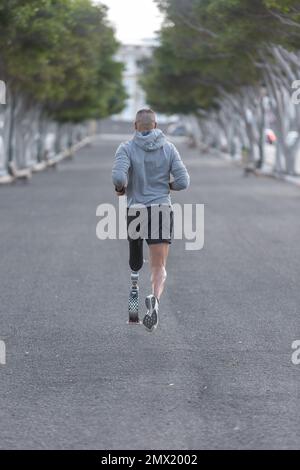 Rückblick auf einen unbekannten Sportler mit Beinprothesen, der während des Fitnesstrainings im Park im Sommer auf Asphaltstraße läuft Stockfoto