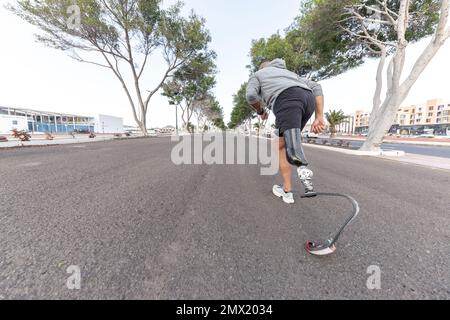 Ganzkörper-anonymer Sportler mit Laufklingenprothese beim Sprinten auf Asphaltpfad während des Fitnesstrainings auf der Straße der Stadt im Sommer Stockfoto