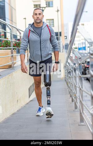 Ganzkörpersportler mit Beinprothesen beim Gehen am Hang außerhalb eines modernen Gebäudes nach einem Fitnesstraining in der Stadt Stockfoto