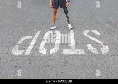 Unerkannter Sportler mit Beinprothese steht auf Asphaltstraße nahe Stop-Inschrift beim Fitnesstraining auf der Stadtstraße Stockfoto