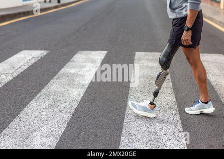 Anonyme Amputierte in Sportbekleidung und Turnschuhe, die während des Fitnesstrainings auf der City Street auf einem Fußgängerüberweg laufen Stockfoto