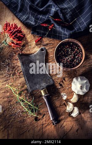 Ein alter Metzger schneidet auf einem Schneidebrett, umgeben von Chili-Paprika, Knoblauch und Rosmarin - Top of view. Stockfoto