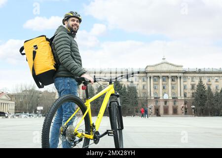 Kurier mit Thermosack und Fahrrad auf der Straße der Stadt. Lebensmittellieferservice Stockfoto