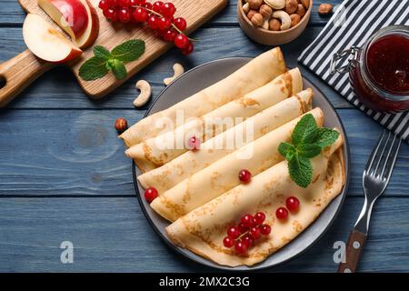 Leckere dünne Pfannkuchen mit Beeren auf blauem Holztisch, flach liegend Stockfoto