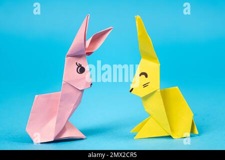 Ein pinkfarbenes und gelbes Origami-Kaninchen auf blauem Hintergrund. Basteln für Ostern, aus Papier falten, selbst machen Stockfoto