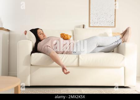 Faule, übergewichtige Frau mit Chips, die zu Hause auf dem Sofa ruht Stockfoto