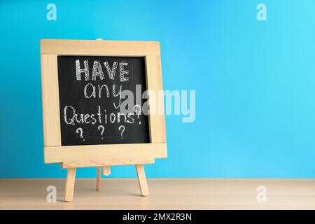 Tafel mit Wortgruppe HALTEN SIE ALLE FRAGEN auf dem Holztisch vor blauem Hintergrund. Platz für Text Stockfoto