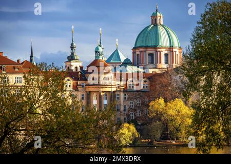 Farbenfrohes Gebäude der Prager Altstadt, Kirche St. Franziskus von Assisi mit grüner Kuppel, gelber Herbstbaum am Ufer, Moldau, Tschechische republik Stockfoto