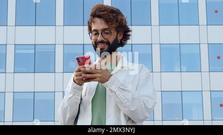 Ein junger, lächelnder italienischer Mann, der mit einem Mobiltelefon in einer Stadt chattet Stockfoto