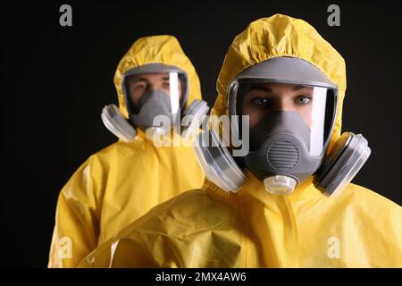 Mann und Frau tragen chemische Schutzanzüge auf schwarzem Hintergrund. Virusforschung Stockfoto