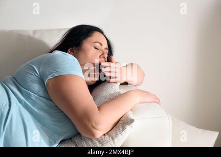 Faule, übergewichtige Frau, die sich zu Hause auf dem Sofa ausruht Stockfoto