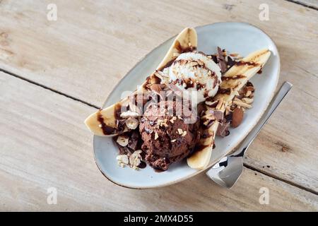 Von oben von süßen Banane Split Dessert mit Vanille und Schokolade Kugeln Eis auf Holztisch serviert Stockfoto