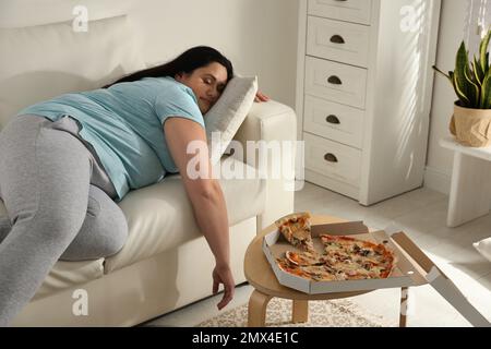 Faule, übergewichtige Frau, die sich zu Hause neben Pizza auf dem Tisch ausruht Stockfoto