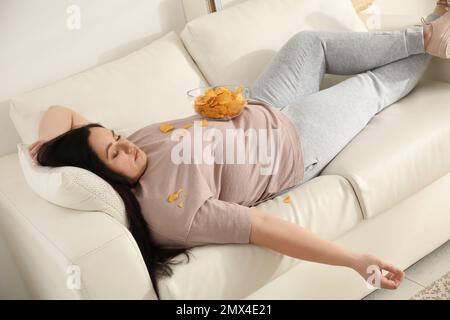 Faule, übergewichtige Frau mit Chips, die zu Hause auf dem Sofa ruht Stockfoto