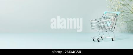 Einkaufsbanner mit Trolley auf blauem Hintergrund mit weißen Blumen und Kopierbereich. Frühlingssaison-Sonderangebot, Shopping im Supermarkt-Konzept. Bannergröße Stockfoto