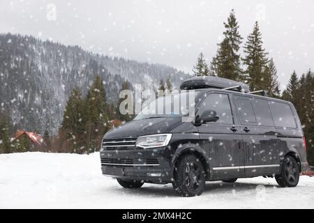 Schwarzes Auto auf verschneiter Straße. Winterurlaub Stockfoto
