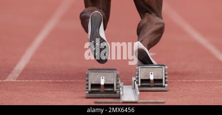 Männerfüße des Sportlers auf Startblock, bereit für einen Sprintstart Stockfoto