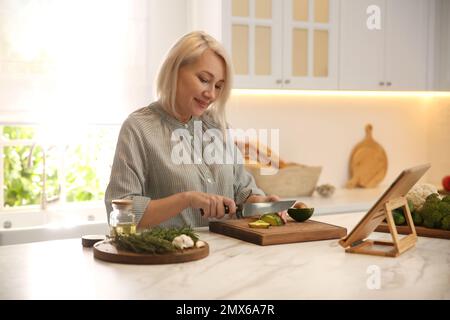 Frau mit Tablet, die am Tisch in der Küche kocht Stockfoto