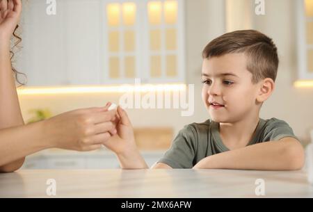 Eine afroamerikanische Frau, die dem kleinen Jungen in der Küche eine Vitaminpille gibt Stockfoto