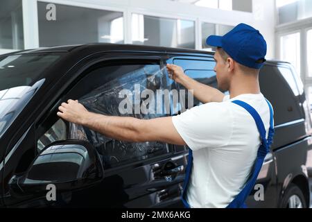 Arbeiter, der Autofenster mit Folie in der Werkstatt abfärbt Stockfoto