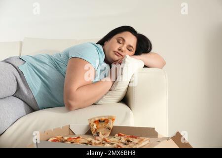 Faule, übergewichtige Frau, die sich zu Hause neben Pizza auf dem Tisch ausruht Stockfoto