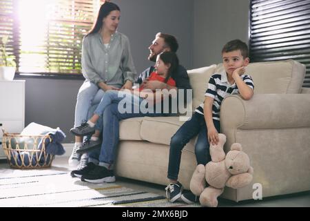 Ein unglücklicher kleiner Junge, der eifersüchtig ist, während die Eltern Zeit mit seiner Schwester zu Hause verbringen Stockfoto