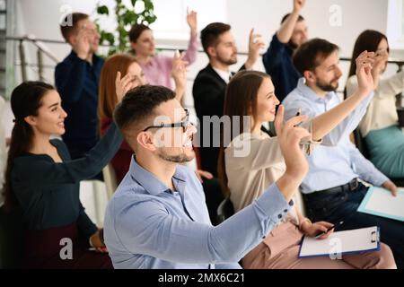 Menschen, die sich bei Geschäftsschulungen in geschlossenen Räumen die Hand heben, um Fragen zu stellen Stockfoto