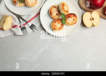 Leckere Hüttenkäse-Pfannkuchen und Äpfel auf grauem Marmortisch, flach liegend. Platz für Text Stockfoto