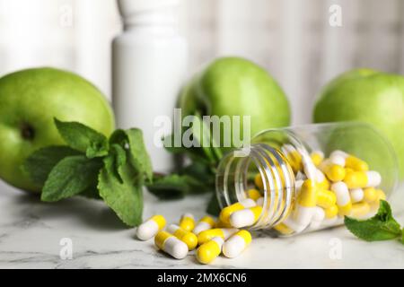 Flasche mit Vitaminpillen, Äpfeln und Minze auf weißem Marmortisch Stockfoto