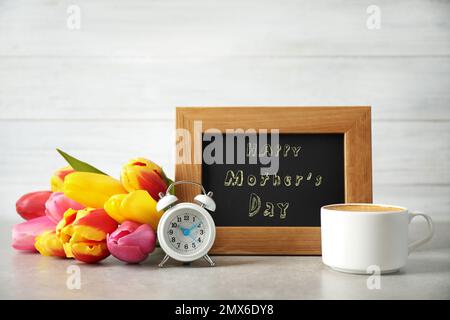 Tafel mit Satz HAPPY MOTHER's DAY, Tulpen, Tasse Kaffee und Wecker auf Lichttisch Stockfoto