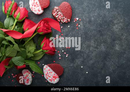 Rote Samt- oder Brownie-Kekse in Herzform in Schokoladeneis mit roten Rosen auf schwarzem Hintergrund. Dessert-Idee für Valentinstag, Mütter oder Frauen Stockfoto