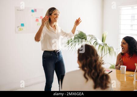 Fröhliche Geschäftsfrau lacht mit ihren Kollegen während eines Meetings in einem Sitzungssaal. Multikulturelle Geschäftsfrauen feiern ihren Erfolg. Geschäftsauftrag Stockfoto