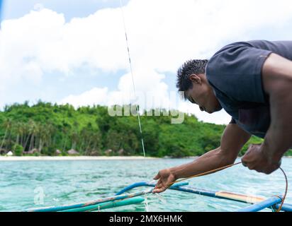 Eine Nahaufnahme eines asiatischen Fischers, der sein Fischernetz auf einem kleinen Boot auf dem Meer, auf den Philippinen Inseln, auf dem Lebensstil aufhebt Stockfoto