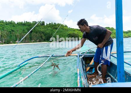 Asiatischer Fischer, der sein Fischernetz auf einem kleinen Boot auf See mit Kopierraum, philippinischen Inseln, Lifestyle Stockfoto