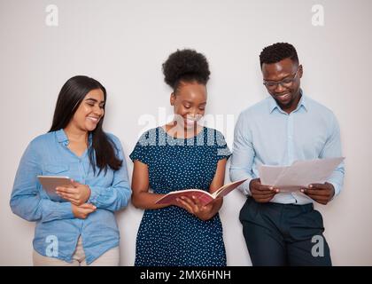 Drei verschiedene Kollegen lehnen sich gegen eine Wand und teilen sich Notizen und berichten über Lachen Stockfoto