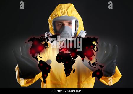 Mann in chemischem Schutzanzug und Weltkarte auf schwarzem Hintergrund. Virus verbreitet Stockfoto