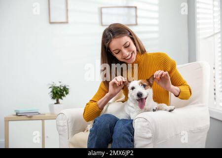 Junge Frau mit ihrem süßen Jack Russell Terrier im Sessel zu Hause. Hübsches Haustier Stockfoto