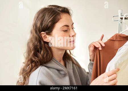 Gebrauchte Kleidung an Kleiderbügeln. Die Frau sucht sich Kleidung im Laden aus Stockfoto