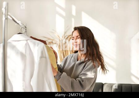 Gebrauchte Kleidung an Kleiderbügeln. Die Frau wählt Kleidung aus zweiter Hand Stockfoto