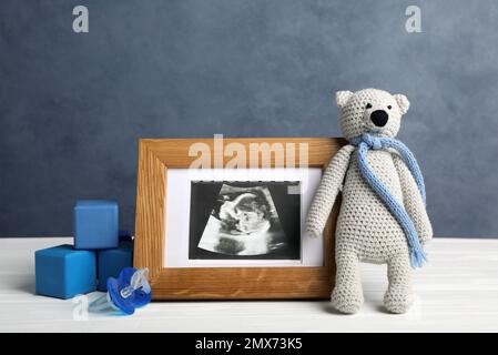 Komposition mit kindlichem Ultraschallfoto und Spielzeug auf dem weißen Tisch Stockfoto