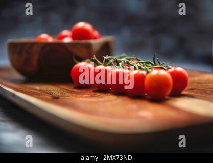 Aromatico-Tomaten auf Holzplatte, einige auf Weinrebe, andere in einer Holzschüssel. Stockfoto